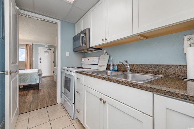 kitchen with sink, white cabinetry, dark stone countertops, light tile patterned floors, and white electric stove