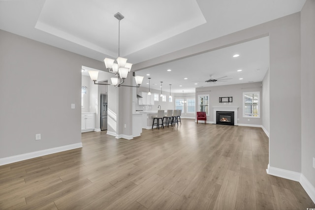 unfurnished living room featuring a tray ceiling, light hardwood / wood-style flooring, and ceiling fan with notable chandelier