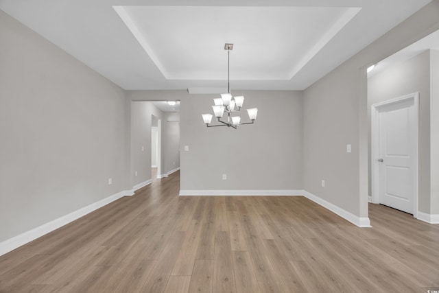 spare room featuring light hardwood / wood-style floors, a raised ceiling, and a chandelier