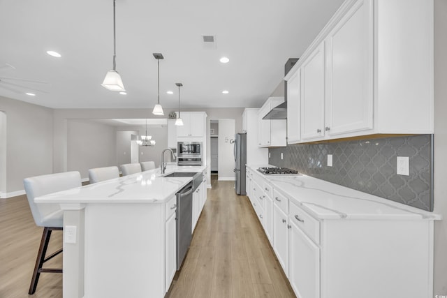 kitchen featuring a breakfast bar, white cabinetry, decorative light fixtures, a large island with sink, and stainless steel appliances