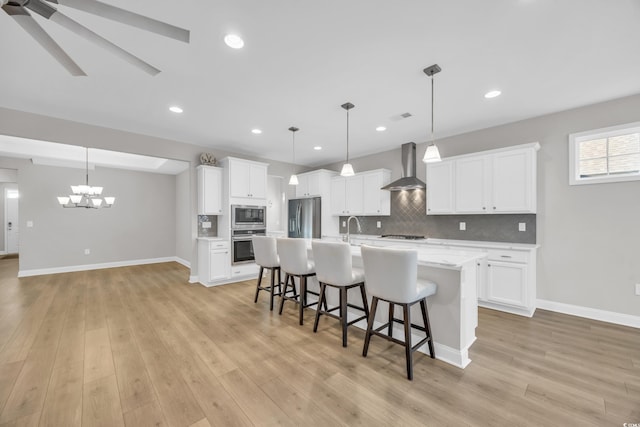 kitchen featuring appliances with stainless steel finishes, decorative light fixtures, wall chimney range hood, and white cabinets