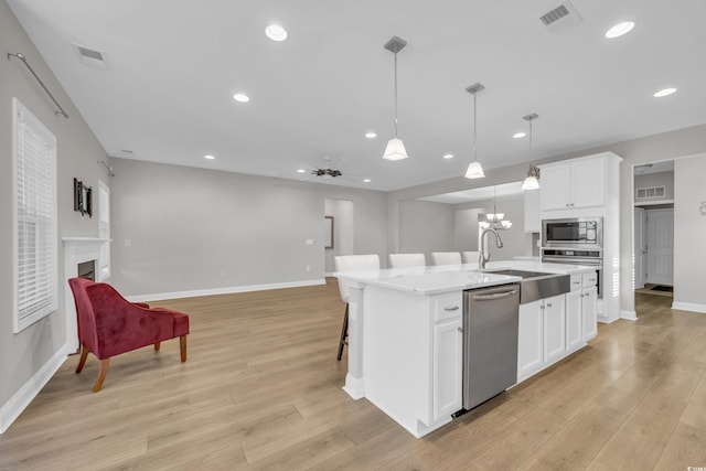 kitchen with appliances with stainless steel finishes, decorative light fixtures, an island with sink, sink, and white cabinets