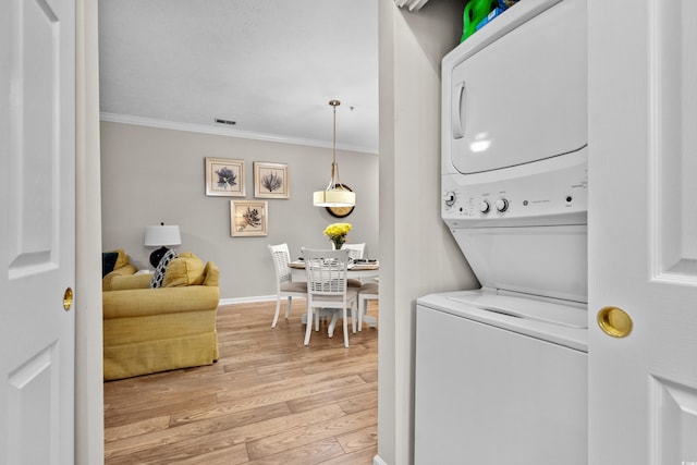 washroom with hardwood / wood-style flooring, stacked washer / dryer, and crown molding