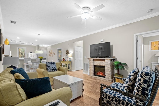 living room with ornamental molding, a stone fireplace, light hardwood / wood-style flooring, and a textured ceiling