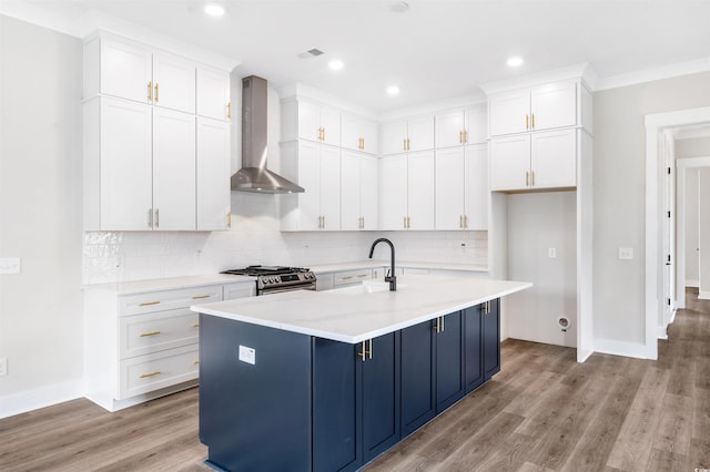 kitchen featuring sink, white cabinetry, stainless steel range with gas stovetop, a center island with sink, and wall chimney exhaust hood