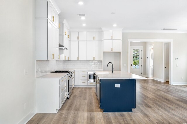 kitchen with an island with sink, blue cabinetry, white cabinetry, hanging light fixtures, and stainless steel microwave