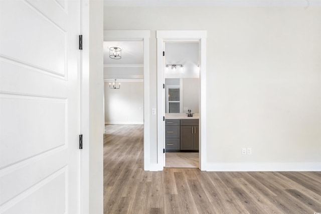 hallway with crown molding, sink, a notable chandelier, and light hardwood / wood-style flooring