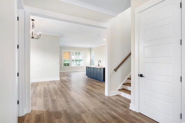 corridor featuring sink, a notable chandelier, light hardwood / wood-style flooring, and ornamental molding