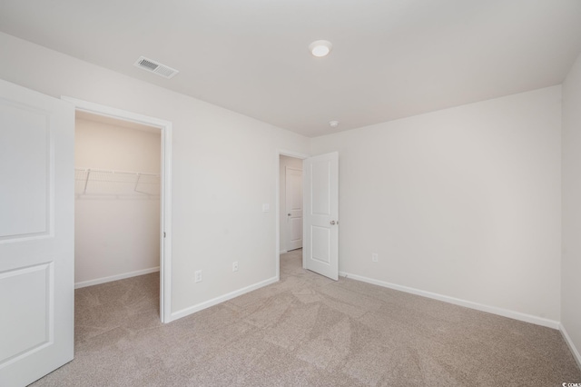unfurnished bedroom featuring a spacious closet, baseboards, light colored carpet, and visible vents