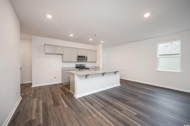kitchen featuring appliances with stainless steel finishes, baseboards, dark wood-type flooring, visible vents, and a center island with sink