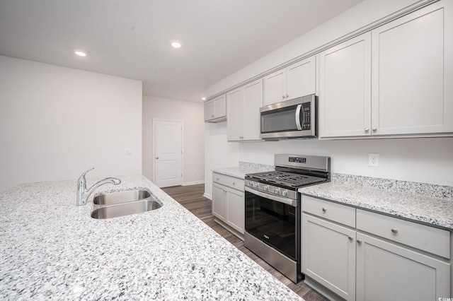 kitchen with a sink, light stone counters, stainless steel appliances, and dark wood finished floors