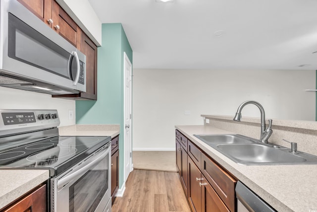 kitchen featuring a sink, light wood-style floors, light countertops, appliances with stainless steel finishes, and brown cabinetry