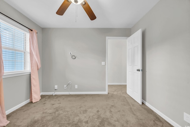 spare room with a ceiling fan, light carpet, and baseboards