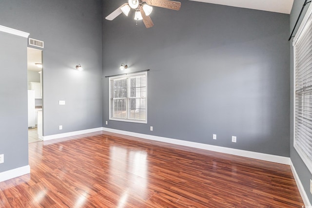 empty room featuring hardwood / wood-style flooring, ceiling fan, and a towering ceiling