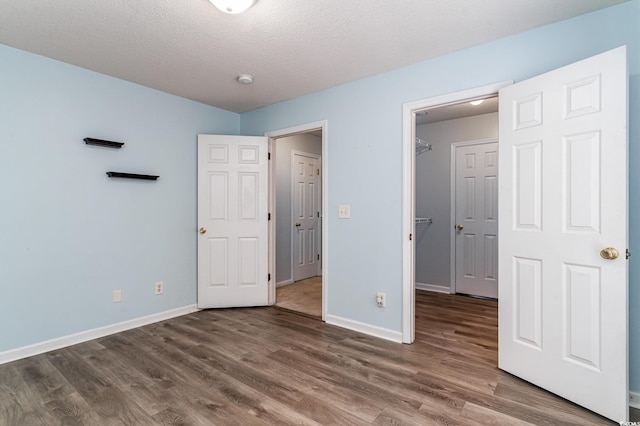 unfurnished bedroom featuring dark hardwood / wood-style flooring, a spacious closet, and a textured ceiling