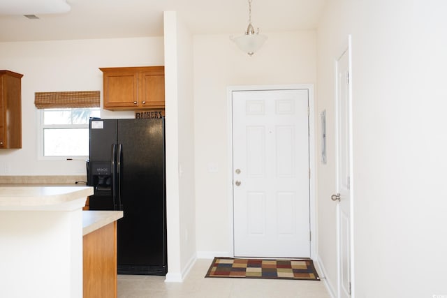 kitchen featuring baseboards, light countertops, hanging light fixtures, black refrigerator with ice dispenser, and brown cabinetry