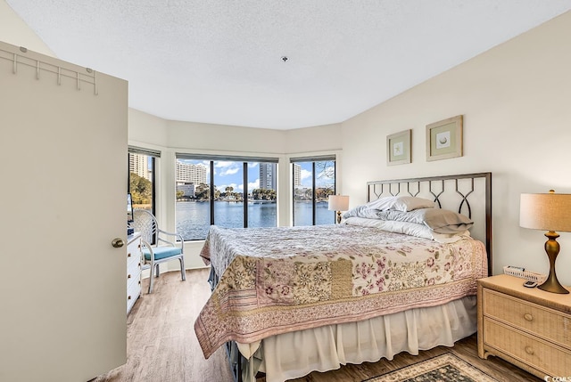 bedroom with a water view, light hardwood / wood-style floors, and a textured ceiling