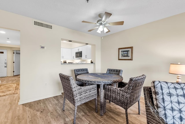 dining space with ceiling fan, a textured ceiling, and light wood-type flooring