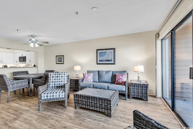 living room featuring ceiling fan, light hardwood / wood-style floors, and a textured ceiling