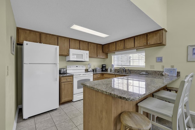 kitchen featuring sink, white appliances, light tile patterned floors, a breakfast bar, and kitchen peninsula