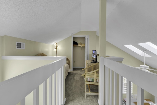 hallway with carpet flooring, vaulted ceiling with skylight, and a textured ceiling