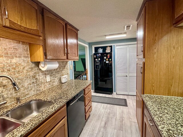 kitchen with stone countertops, light hardwood / wood-style floors, sink, and black appliances