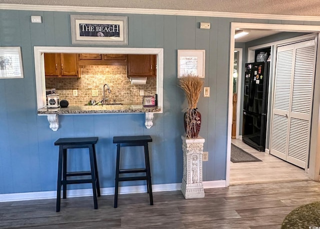 kitchen featuring sink, a breakfast bar area, black fridge, crown molding, and stone countertops