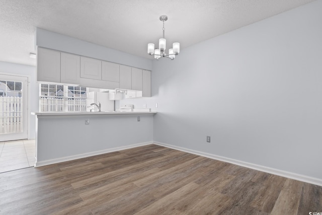 kitchen with a chandelier, hardwood / wood-style flooring, kitchen peninsula, pendant lighting, and white cabinets