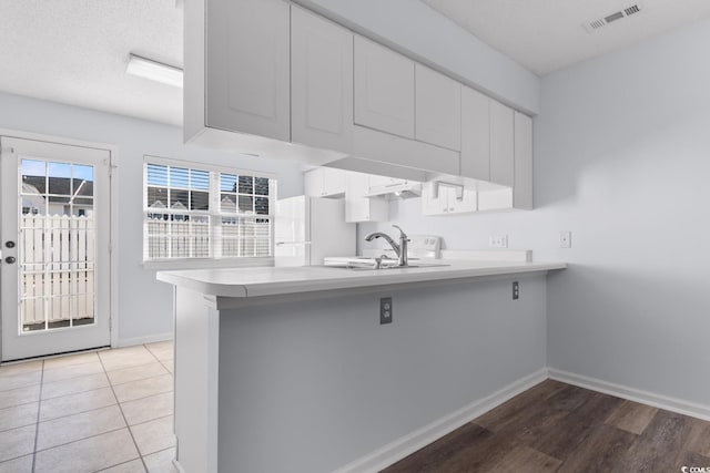 kitchen featuring sink, white cabinets, white refrigerator, kitchen peninsula, and a textured ceiling