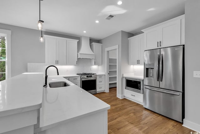 kitchen featuring premium range hood, sink, white cabinetry, appliances with stainless steel finishes, and kitchen peninsula