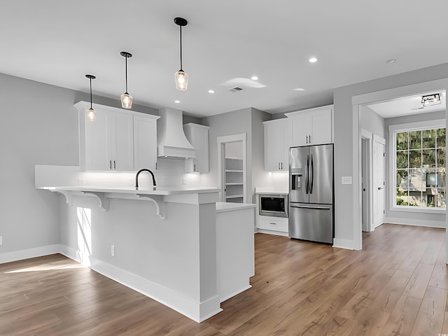 kitchen with decorative light fixtures, appliances with stainless steel finishes, kitchen peninsula, custom range hood, and white cabinets