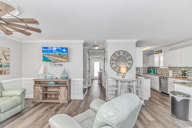 living room with sink, crown molding, light hardwood / wood-style flooring, ceiling fan, and a textured ceiling