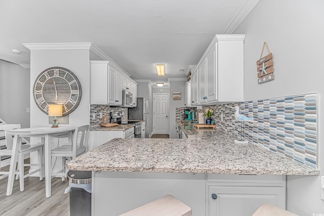 kitchen featuring ornamental molding, stainless steel appliances, kitchen peninsula, and white cabinets