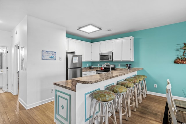 2022 N Waccamaw Dr, Garden City Beach, SC 29576 - kitchen featuring stainless steel appliances, a peninsula, light wood-style flooring, baseboards, and white cabinets