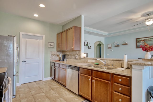 kitchen featuring arched walkways, stainless steel appliances, a sink, brown cabinets, and tasteful backsplash