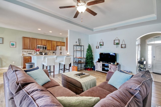 living room with arched walkways, ceiling fan, recessed lighting, light wood-style floors, and a tray ceiling