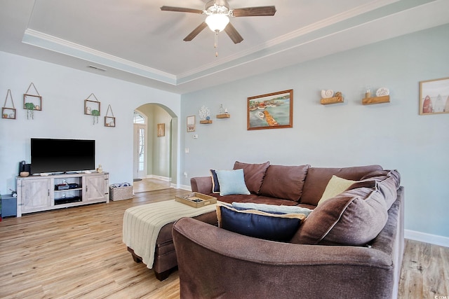 living area with a tray ceiling, arched walkways, light wood finished floors, ceiling fan, and baseboards