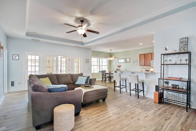 living area with a tray ceiling, ceiling fan, light wood-style flooring, and baseboards