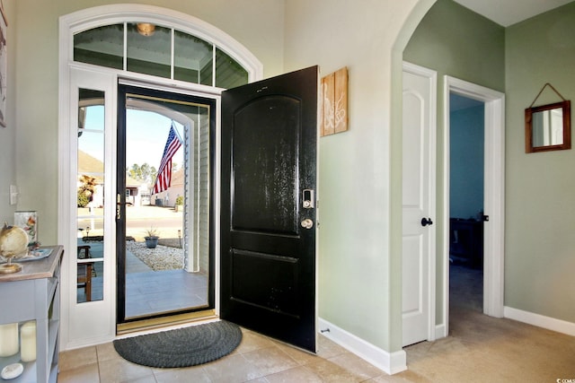 entryway with light carpet, light tile patterned floors, baseboards, and arched walkways