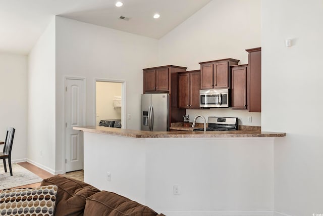 kitchen with a towering ceiling, stainless steel appliances, kitchen peninsula, and dark brown cabinetry