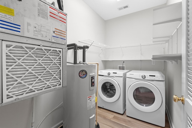 clothes washing area featuring electric water heater, washer and dryer, and light hardwood / wood-style floors