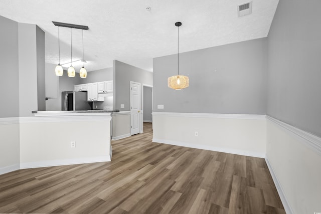 kitchen featuring stainless steel refrigerator, decorative light fixtures, hardwood / wood-style floors, and white cabinets