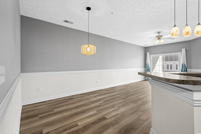 unfurnished dining area with a textured ceiling, dark wood-type flooring, and ceiling fan