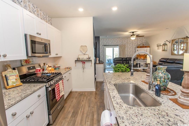 kitchen with sink, white cabinetry, light stone counters, stainless steel appliances, and light hardwood / wood-style floors