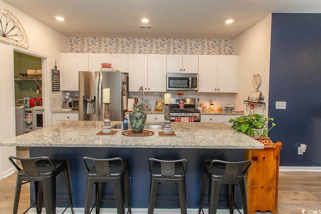 kitchen featuring stainless steel appliances, white cabinetry, and a center island with sink