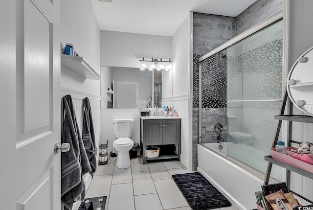 full bathroom featuring shower / bath combination with glass door, vanity, a textured ceiling, tile patterned floors, and toilet