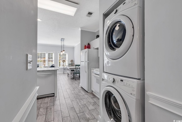 laundry room featuring crown molding, a textured ceiling, and stacked washing maching and dryer