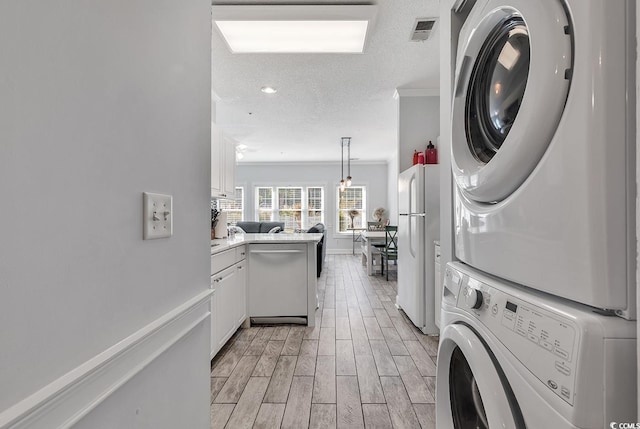 laundry room featuring crown molding, stacked washer and clothes dryer, and a textured ceiling