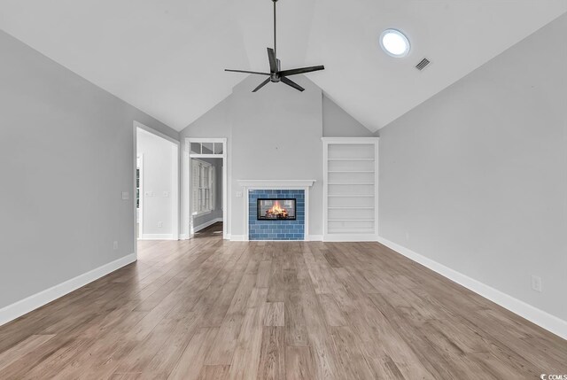 unfurnished living room with ceiling fan, high vaulted ceiling, a tile fireplace, and light hardwood / wood-style flooring