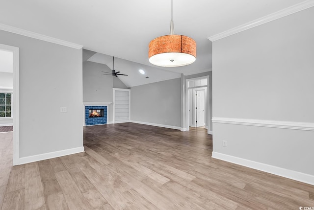 unfurnished living room featuring ceiling fan, ornamental molding, a tiled fireplace, vaulted ceiling, and light wood-type flooring